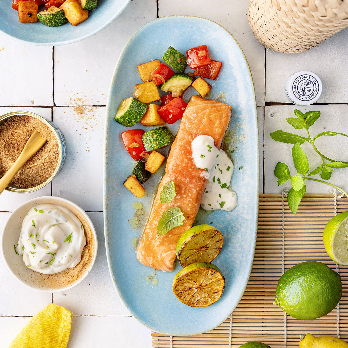 Sommerlicher Caipi-Lachs mit Limetten, Minze und mediterranem Gemüse auf hellblauem Teller.