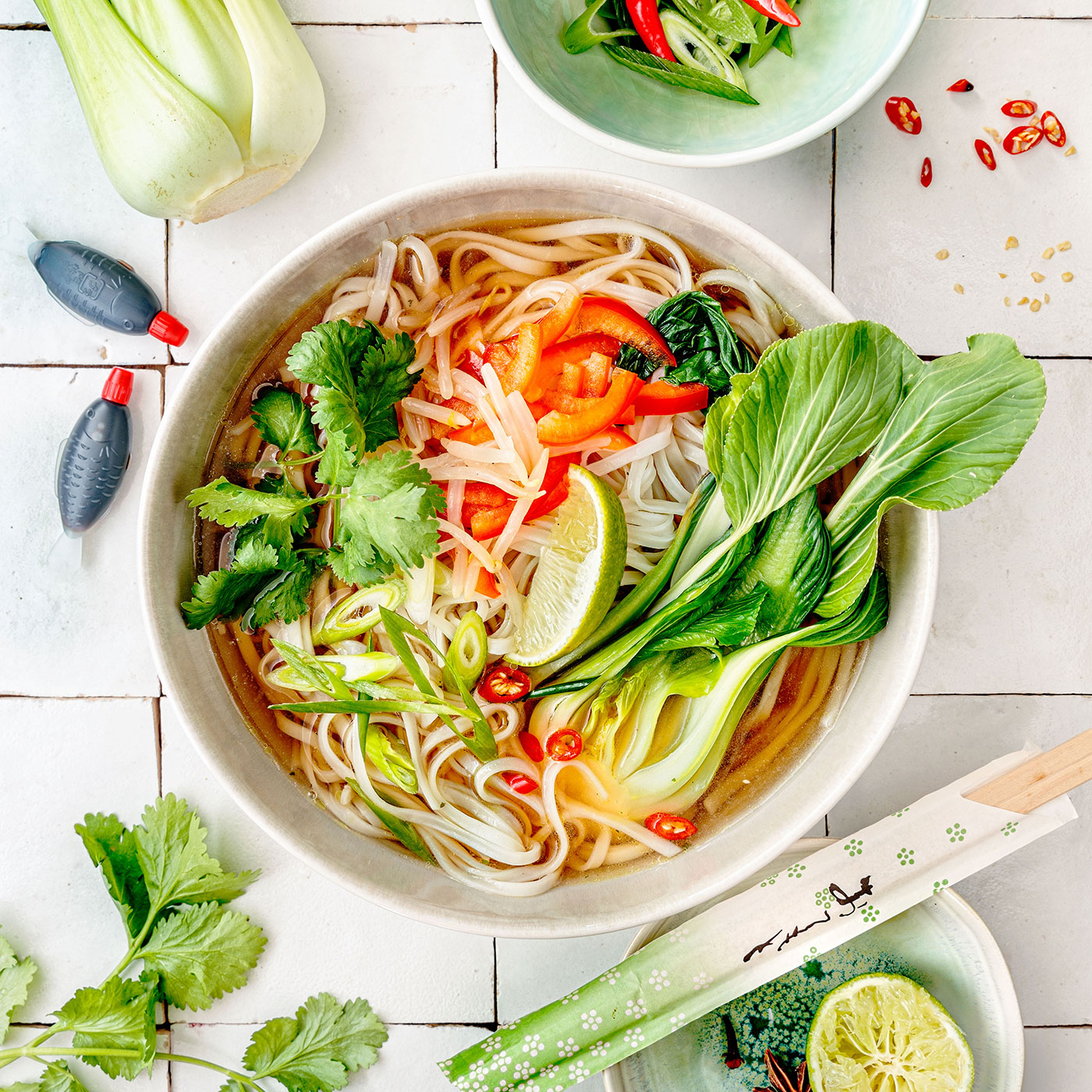 Vietnamesische Pho mit Reisnudeln, Pak Choi, Chili, Limette und frischen Kräutern in einer hellen Schale.