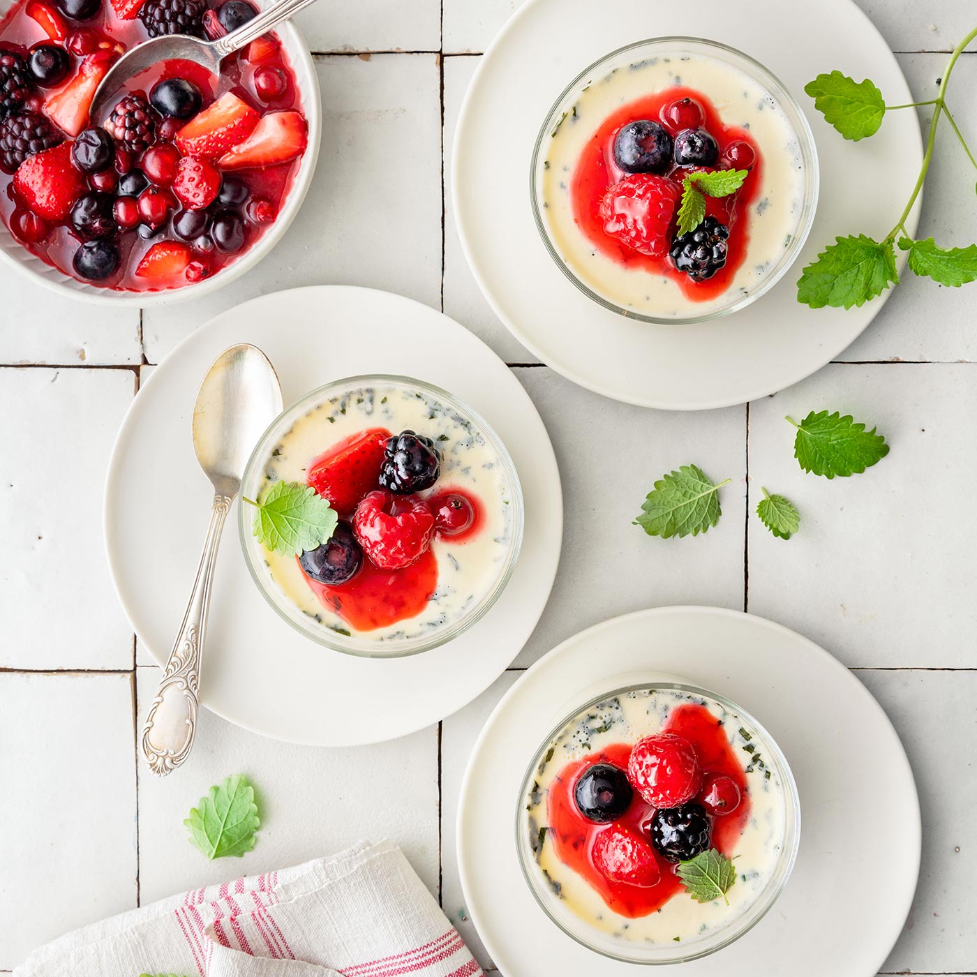 Panna Cotta mit Zitronenmelisse und frischem Beerenkompott in Glasdesserts, hell und festlich angerichtet.