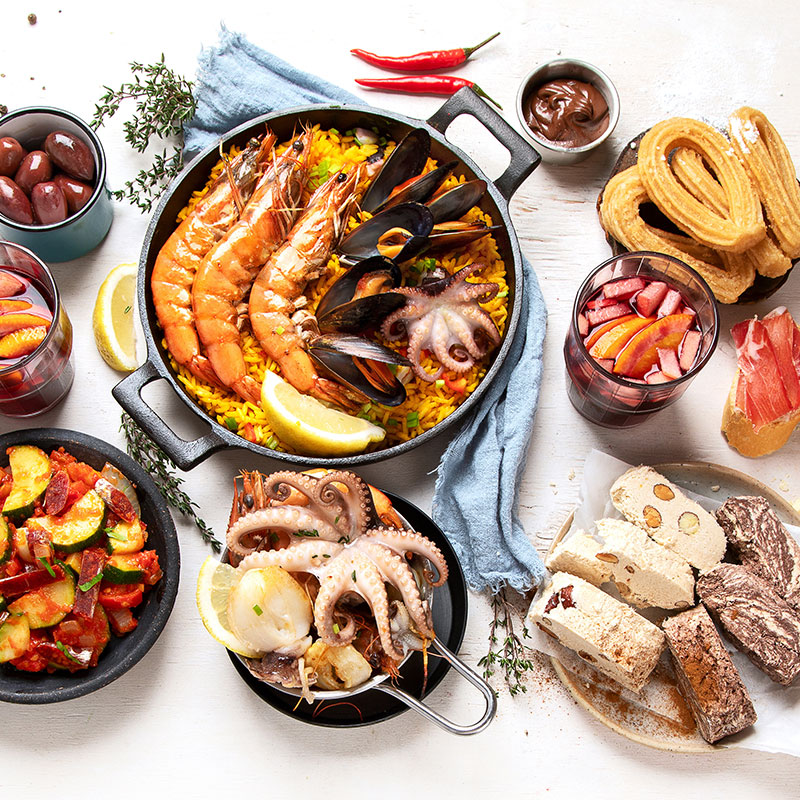 Spanisches Weihnachtsessen mit Paella, Meeresfrüchten, Turrón und Churros auf festlich gedecktem Tisch.