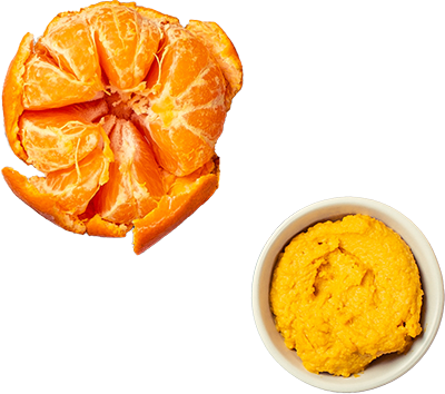 Aufgebrochene Mandarine mit Schale, daneben Schale mit Püree und zwei Zuckerstangen auf hellem Untergrund.