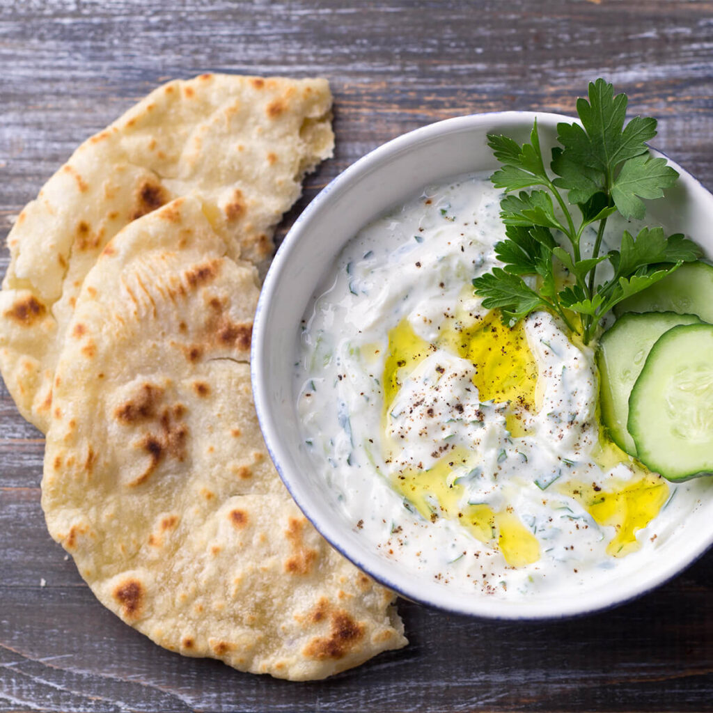 Pitabrot und eine Schale mit Tzatziki-dip garniert mit frischer Gurke und Blattpetersilie