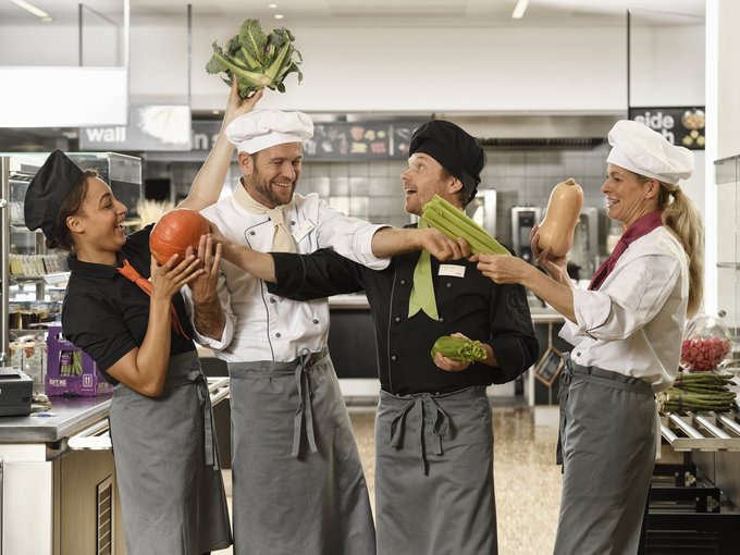 Küchenteam von apetito catering hat Spaß bei der Arbeit, spielt mit frischem Gemüse und freut sich auf die Verpflegung der Gäste und Mitarbeiter 