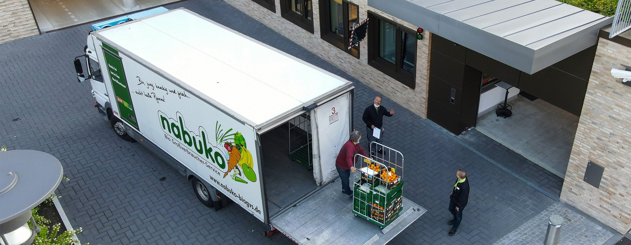 Ein beige, graues Firmengelände. Im Innenhof ein weißer LKW der Firma nabuko. Diese laden Obst und Gemüse aus 