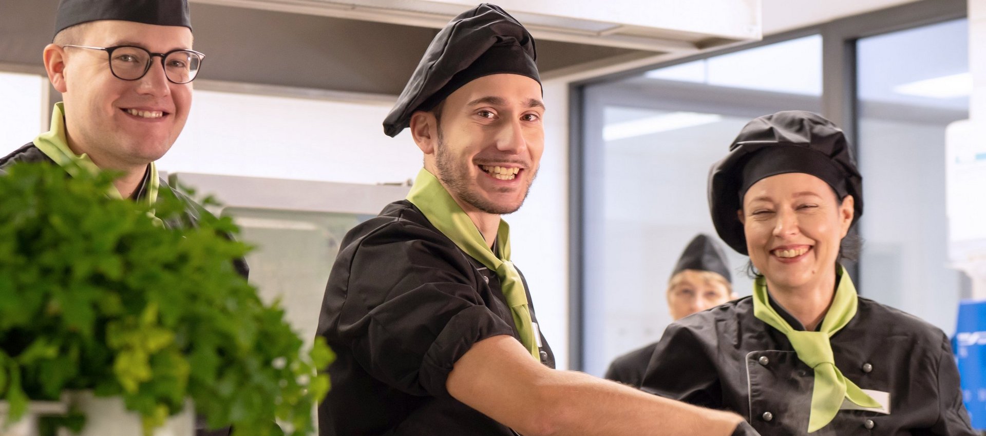 Drei Küchenmitarbeiter lächeln bei der Arbeit im Catering für Betriebe