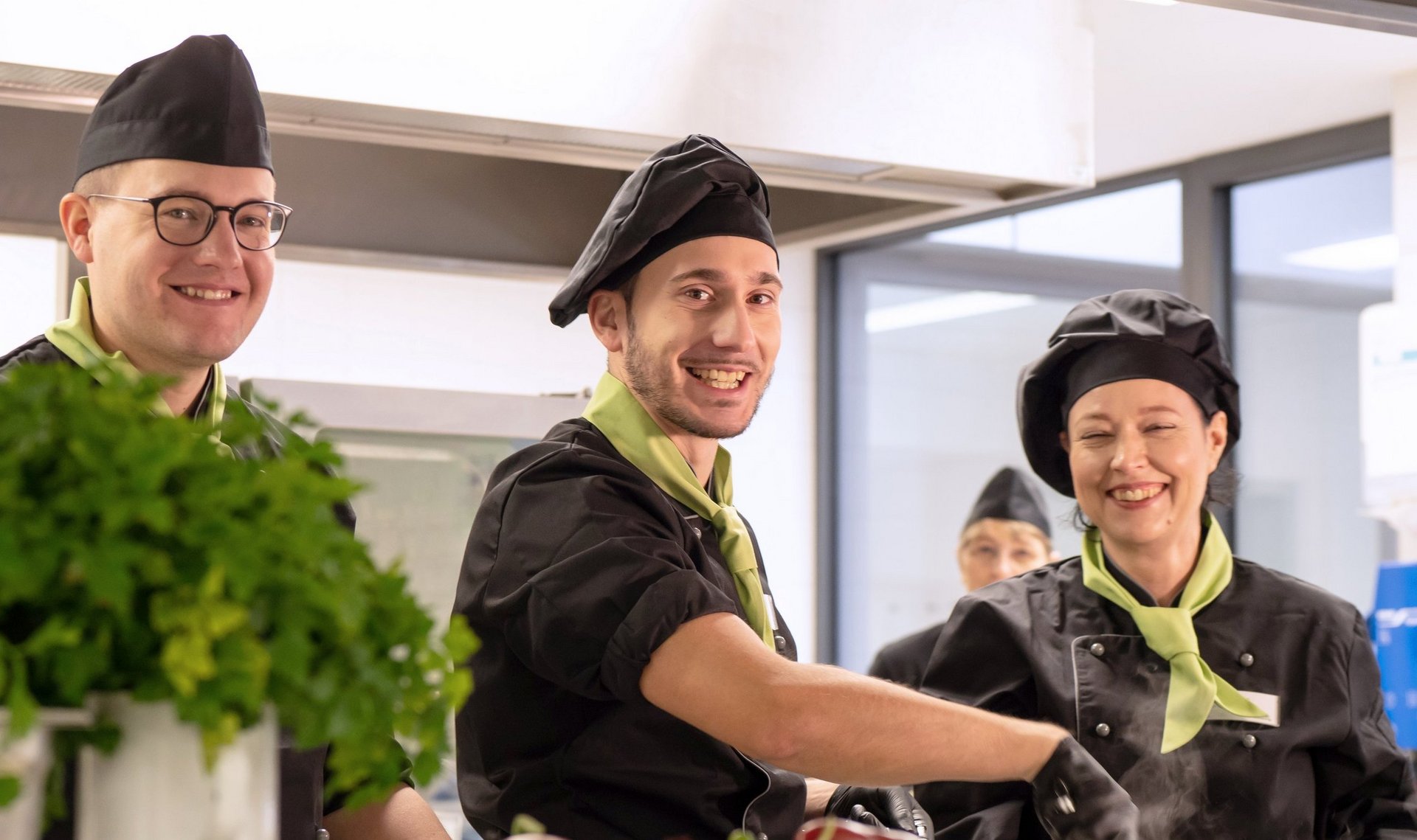 Drei Küchenmitarbeiter lächeln bei der Arbeit im Catering für Betriebe