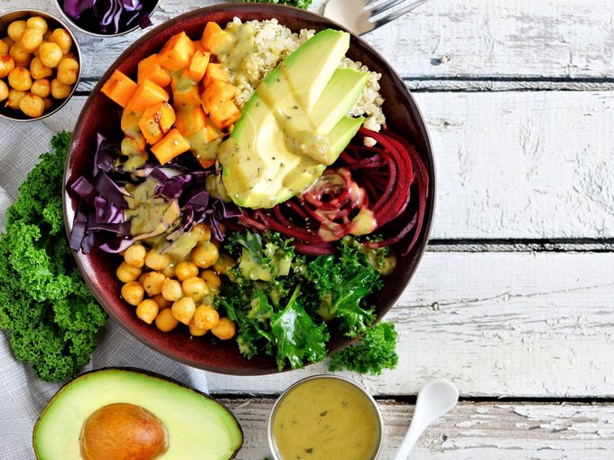 Bowl mit Avocado, Kichererbsen, Salat und verschiedenen Soßen auf einem Holztisch angerichtet