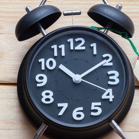Schwarzer und großer Wecker zeigt Uhrzeit an und liegt auf einem Holztisch