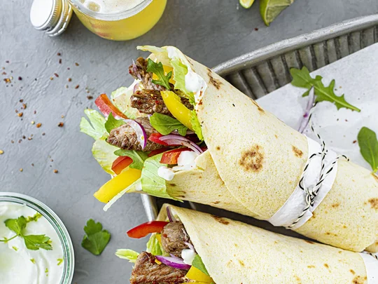 Gesunde Wraps mit Fleisch, Paprika, Zwiebeln und Salat angerichtet mit Kräuterdip und Limonade