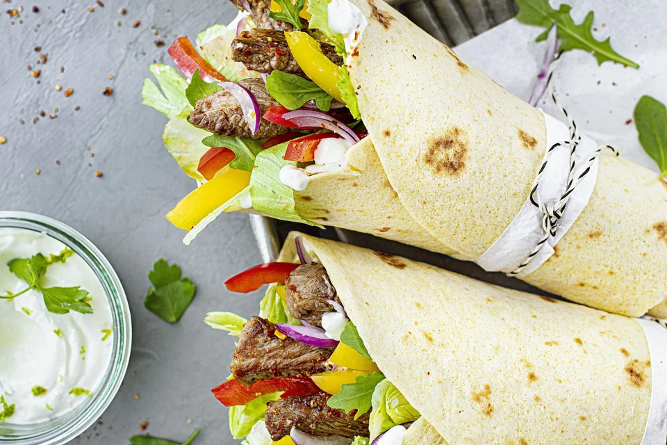 Gesunde Wraps mit Fleisch, Paprika, Zwiebeln und Salat angerichtet mit Kräuterdip und Limonade