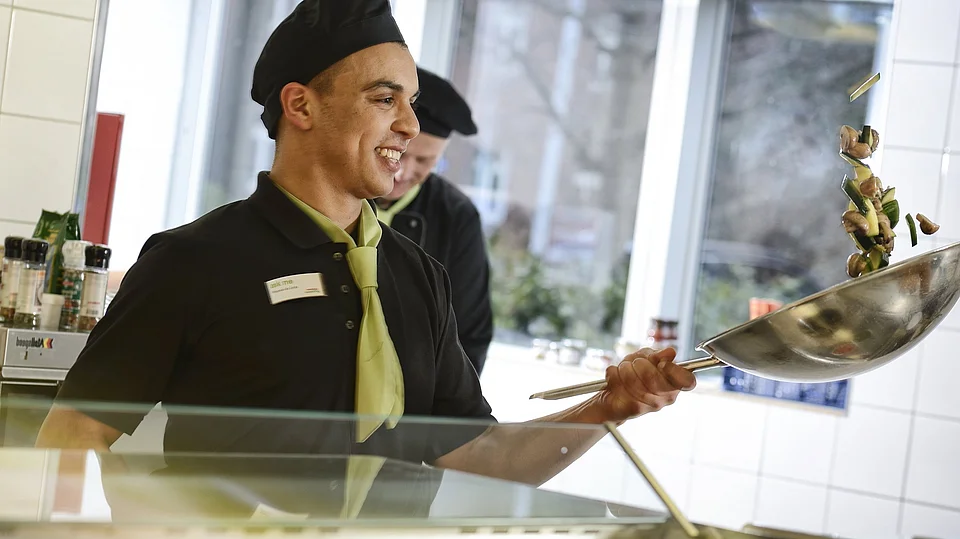 Koch schwingt seine Gemüsepfanne und bereitet Essen für Betriebe zu