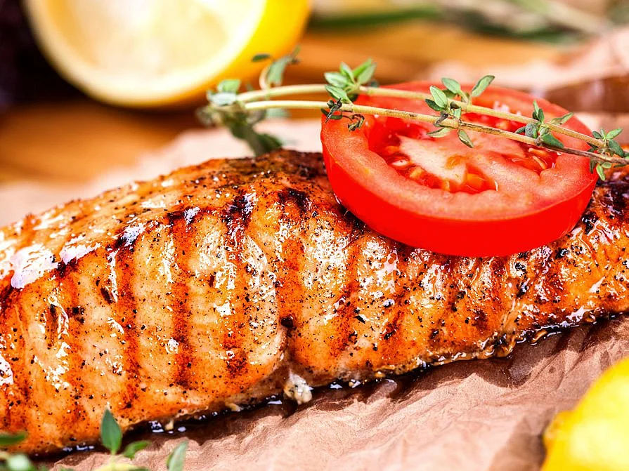Saftiger Lachs garniert mit einer Tomatenscheibe und frischen Kräutern
