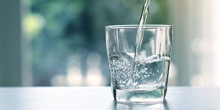 Glas Wasser steht auf einem Tisch und wird befüllt