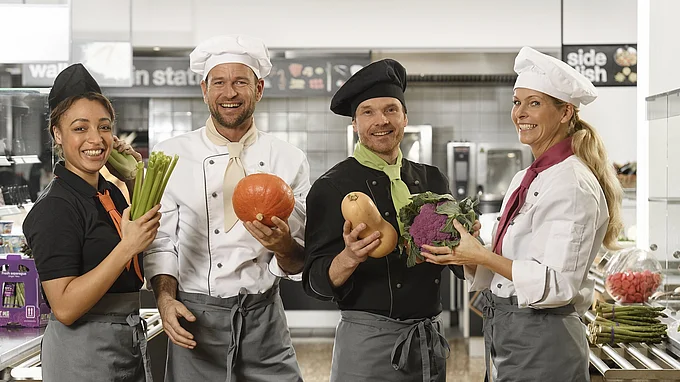Küchenteam von apetito catering mit frischem Gemüse freut sich auf die Verpflegung der Gäste und Mitarbeiter 