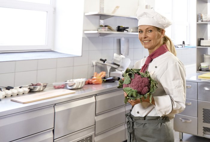 Care Gastronomie Mitarbeiterin mit frischem Blumenkohl in der Hand steht in der Küche