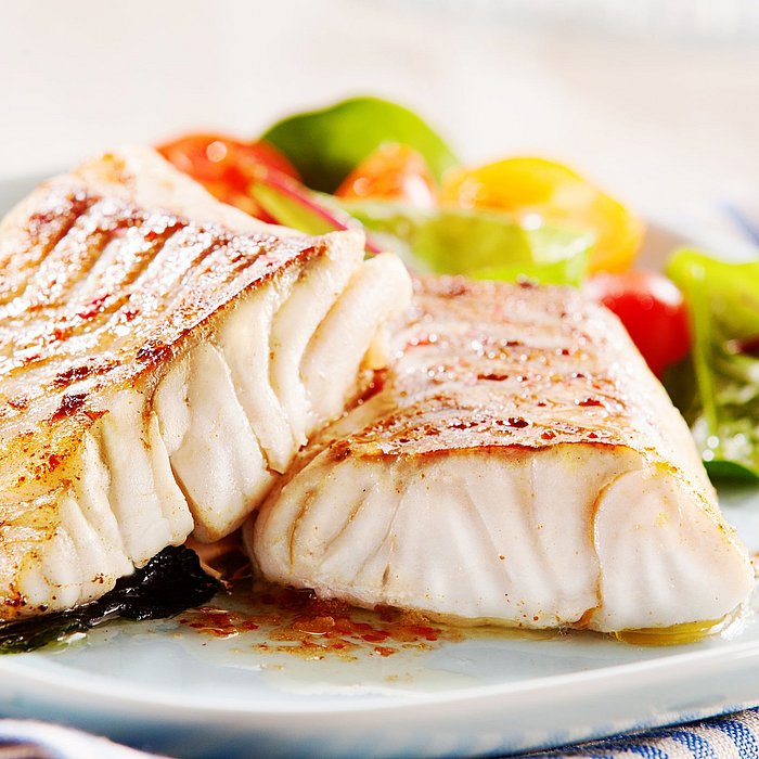 Fisch-Filet an grünem Salat auf einem weißen Teller mit einer blau weiß gestreiften Servierte. Im Hintergrund Kartoffeln